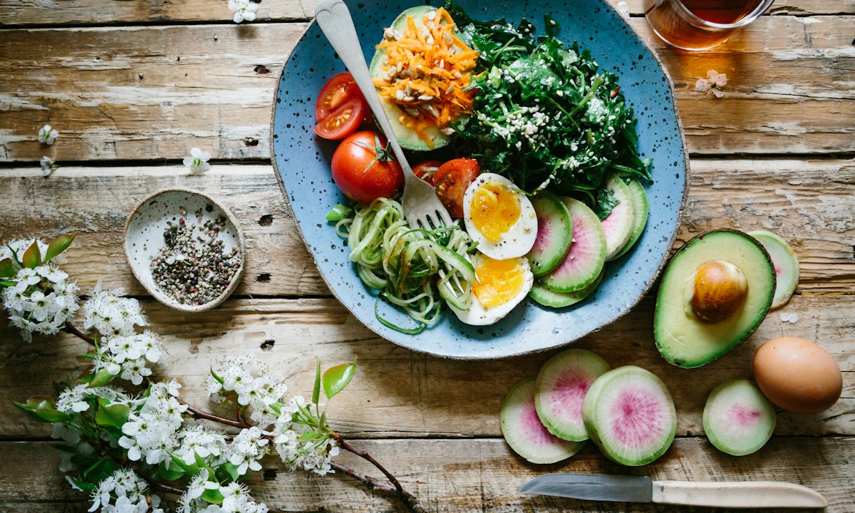 A vegetable plate with egg, avocado and greens on a wooden table